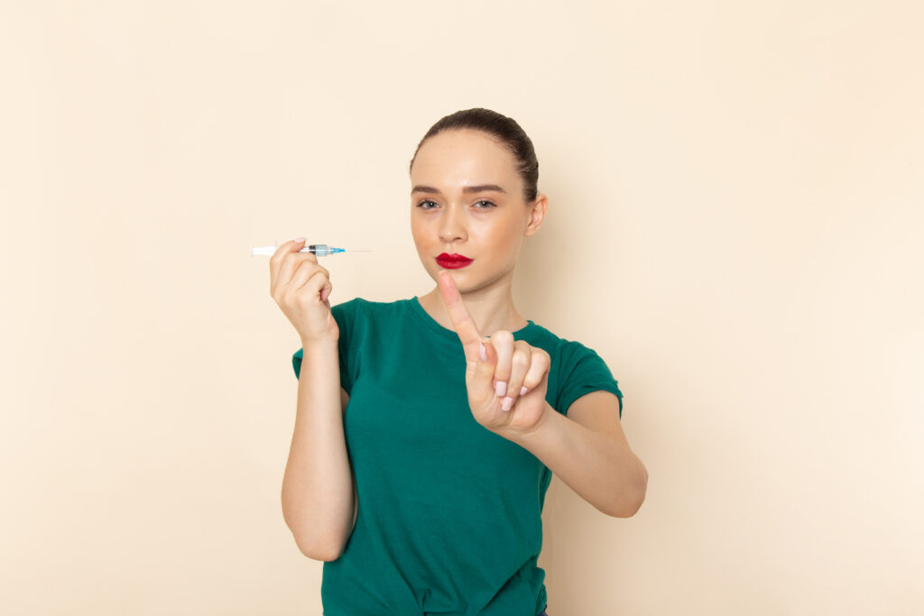front view young female dark green shirt blue jeans holding injection beige desk female model color